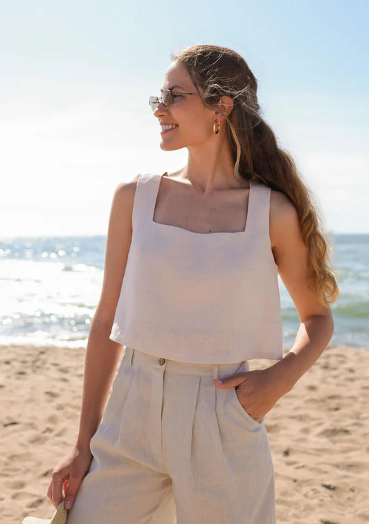 Femme portant un ensemble beige estival avec top sans manches et pantalon large sur une plage ensoleillée